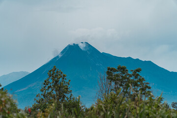The beauty of Mount Merapi from a distance of 13 miles with trees in the foreground. The panoramic beauty of Mount Merapi on a very clear day can be seen very clearly from a distance