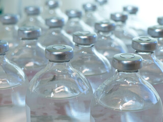 Rows of glass injection bottles with aluminum caps, filled with clear liquid. Medicinal