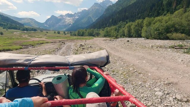 SUV with tourists driving on a stony road in the mountains. First-person view of a man standing in cabin with an open roof. Off-road travelling. Slow motion. Abandonment of tourists in the mountains