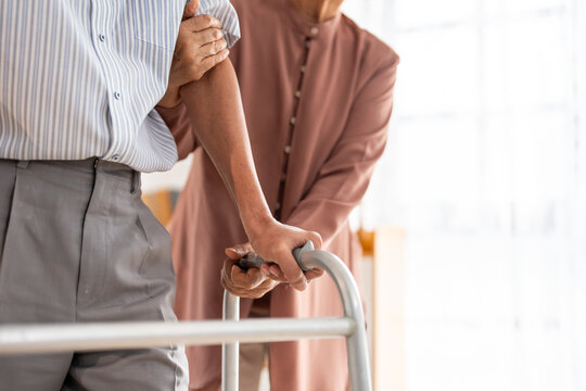 Close up of senior woman's hand support elderly man walking with walker. 