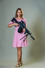 slender beautiful woman in a red dress with a machine gun in her hands on a gray background