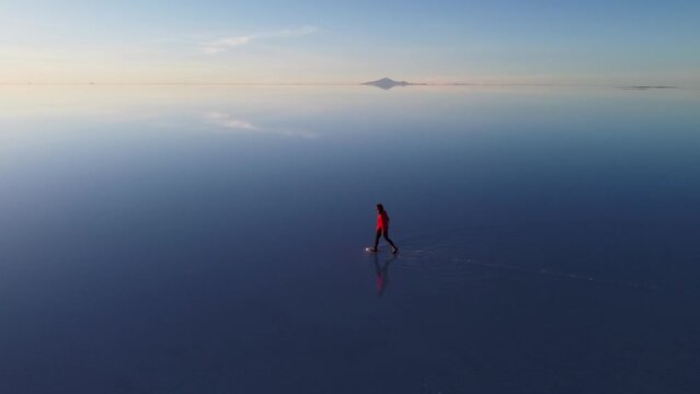 Woman walks on reflective surface of Uyuni Salt Flat, Bolivia aerial