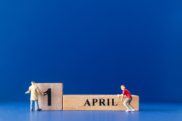 Miniature people painting a wooden block on April 1st, April fools day concept