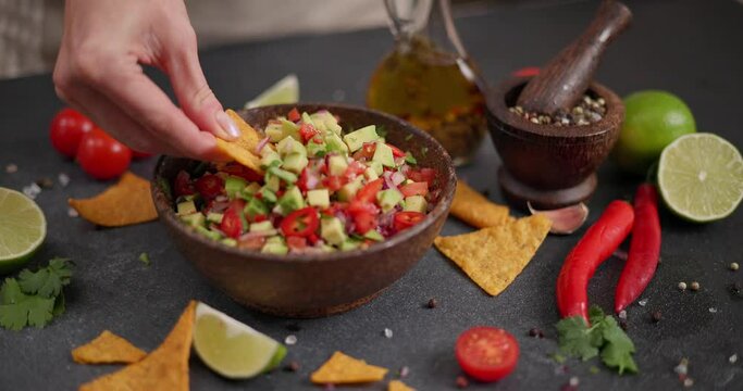 Woman dips tortilla chip into Freshly made salsa dip sauce in a wooden bowl