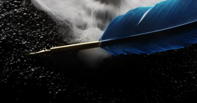 Symbolic blue writing feather sits on black rocks as mythical smoke surrounds it