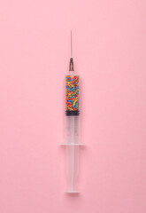 Syringe with sprinkles on a pink background. Party, medicine concept. Minimalism