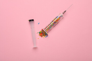 Syringe with sprinkles on a pink background. Party, medicine concept. Minimalism
