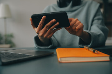 Happy pretty millennial Indian girl relaxing at home, resting in armchair, typing on smartphone, using online app, software, shopping on Internet, making video call. Mobile phone communication