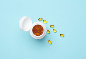 Fish oil capsules in a plastic jar on a blue background. Top view