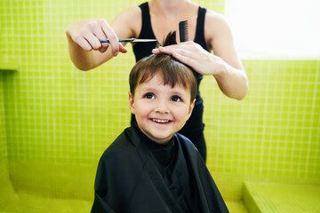 Child, boy and mother with haircut in home for grooming, hairstyle and happiness with scissors. Barber, person and kid for hair treatment, haircare and hairdressing with comb and smile in bathroom