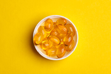 Fish oil capsules on yellow background.