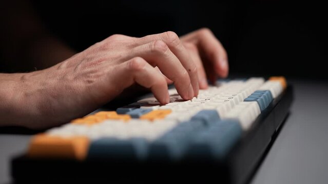 Detail cropped shot of unrecognizable freelancer programmer male typing on wireless mechanical keyboard with stylish colorful keycaps with ASMR thocc sounds, at desk in dark room with cozy light.