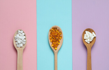 Pills in wooden spoons on colored background