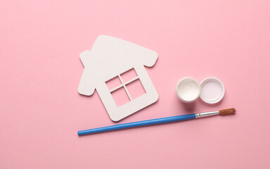 White wooden figurine of house and paint with brush on pink background