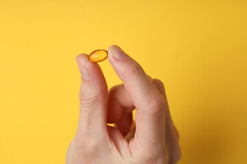 Hand holding fish oil capsule on yellow background
