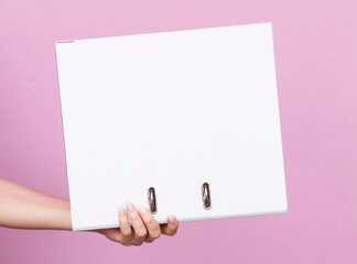 Woman's hand holds white binder with rings on pink background