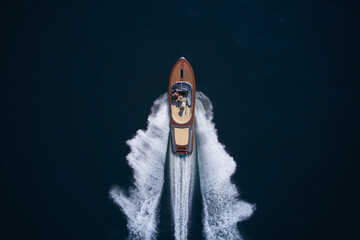 Classic Italian wooden boat fast moving aerial view. Luxurious wooden boat fast movement on dark water. A large modern high-speed wooden luxury boat. Top view of a wooden powerful motor boat.