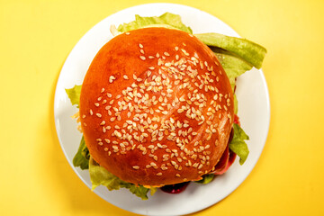 sesame bun, hamburger, on a white plate on a yellow background