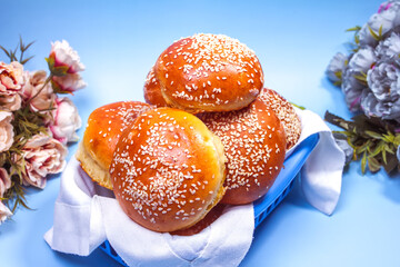 a lot of buns with sesame seeds in a basket on a blue background