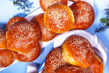 a lot of buns with sesame seeds in a basket on a blue background