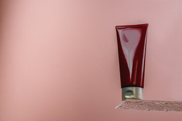 Hair conditioner in a burgundy tube. Shower gel on a glass shelf on a pink background. Hair care....