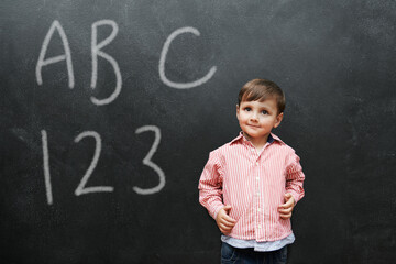 Child, boy and face with smile by blackboard with letters, numbers and happiness in classroom at school. Kid, student and happy for knowledge, learning and chalkboard with math, alphabet or preschool
