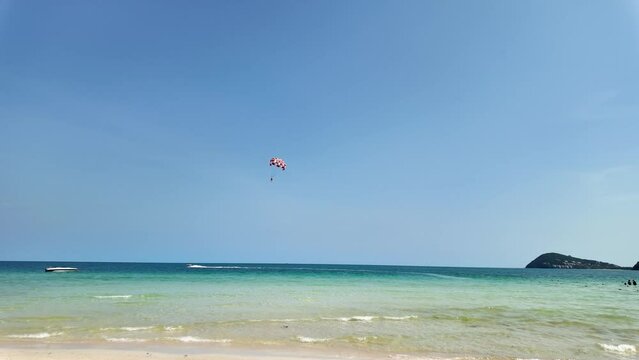 Scenic tropical beach with clear blue skies, a parasailer in the distance, and speedboats near the shore, perfect for travel and summer holiday themes