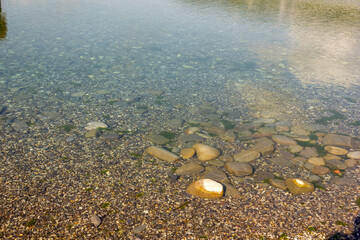 stones and pebbles shine through in clear calm water on the beach at the seashore texture