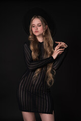Portrait of shy young blonde looking down and crossing arms shyly at elbows. Model poses on black...