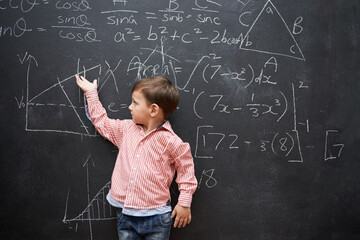 Child, boy and blackboard with math or equations for knowledge, numbers and hand gesture in classroom at school. Kid, student and learning by chalkboard for problem solving, studying and preschool