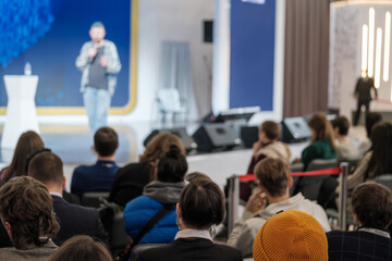 Audience attentively listening to a speaker at a business conference event, with selective focus on...