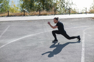 Fototapeta premium Bearded man with long hair doing lunges on the sports field. 