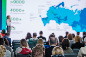 Speaker giving a presentation at a business conference, with attendees listening to global growth strategies.