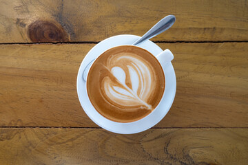 Top down view of delicious golden flat white coffee with tulip latte art in a white cup and saucer on rustic, vintage wooden table