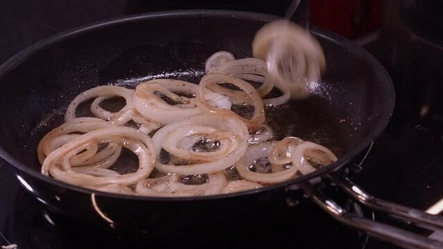 Rings of onion fry in hot frying pan, fork stirs onions sauteed in oil