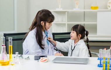 Asian woman doctor and cheerful little girl applying medical stethoscope at doctor appointments in laboratory lab. Education healthcare, medicine childrens hospital concept learning for kids