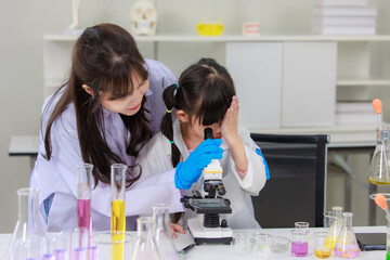Asian woman teacher and little children girl making science experiments tests and looking in microscope at chemical laboratory study room. Education research and development concept learning for kids.