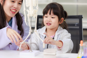 Asian woman doctor physiotherapist explains human fake skeleton hand model on a table to little...