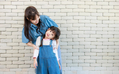 Happy asian beautiful young mother and cute daughter little girl smiling  posing standing on white brick wall background studio portrait Mother's Day love family parenthood childhood concept.