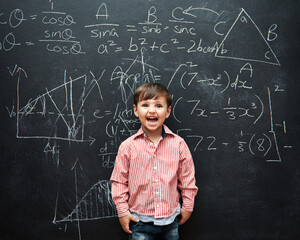 Child, boy and face or excited by blackboard with letters, numbers and education in classroom at school. Kid, student and happy for knowledge, learning and chalkboard with math, drawing and preschool