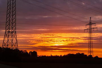Sunset with a dramatic sky and overland high voltage lines near Tabertshausen, Bavaria, Germany