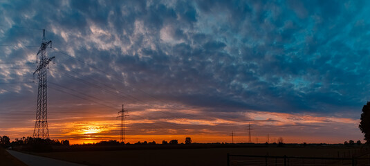 Fototapeta na wymiar Sunset with a dramatic sky and overland high voltage lines near Tabertshausen, Bavaria, Germany