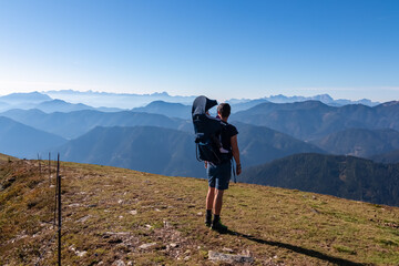 Man with baby carrier looking at magical mountain peaks of Karawanks and Julian Alps seen from Goldeck, Latschur group, Gailtal Alps, Carintha, Austria. Mystical atmosphere in Austrian Alps in summer