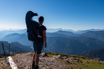 Man with baby carrier looking at magical mountain peaks of Karawanks and Julian Alps seen from...