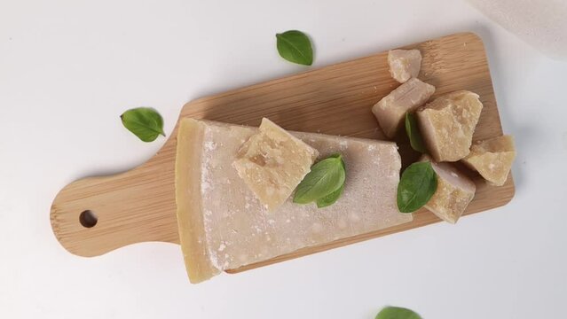 Sprinkle fresh green basil leaves over the Parmesan cheese on the board. A piece of Grana Padano cheese 
