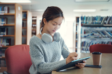 Young asian female college student using digital tablet in college library.