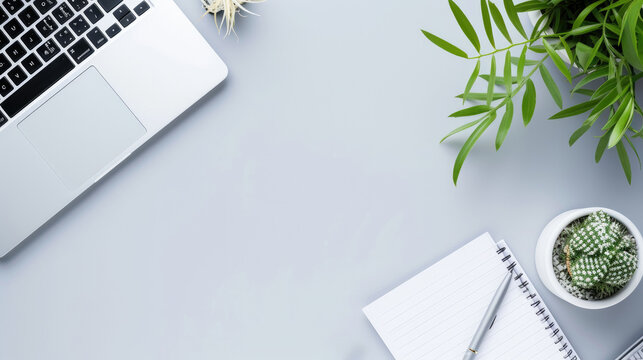 A minimalist workspace featuring a laptop, fresh green plants, and a blank notebook with a pen on a clean, grey background.
