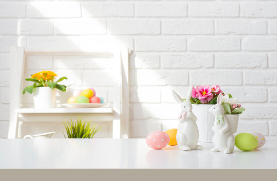 Easter bunnies and painted eggs on table over background of white brick wall with decorated shelf