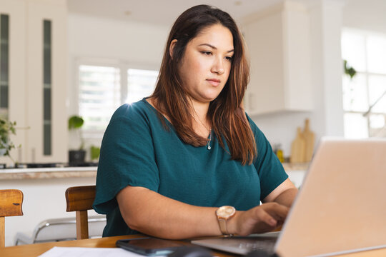 Young plus size biracial woman works diligently on her laptop at home, unaltered - Powered by Adobe