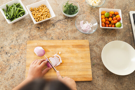 Hands of a person slicing onion on a wooden cutting board in a home kitchen